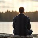 Mies, Ville, istuu meditoimassa kalliolla rauhallisesti, taustalla laaja suomalainen maisema. Hän näyttää syvään keskittyneeltä.